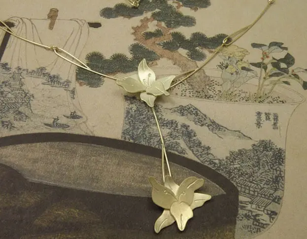 Geelgouden lelies bungelend aan elegante handgemaakte draadschakels. Yellow golden necklace with lillies and handmade chain. Oogst Amsterdam.