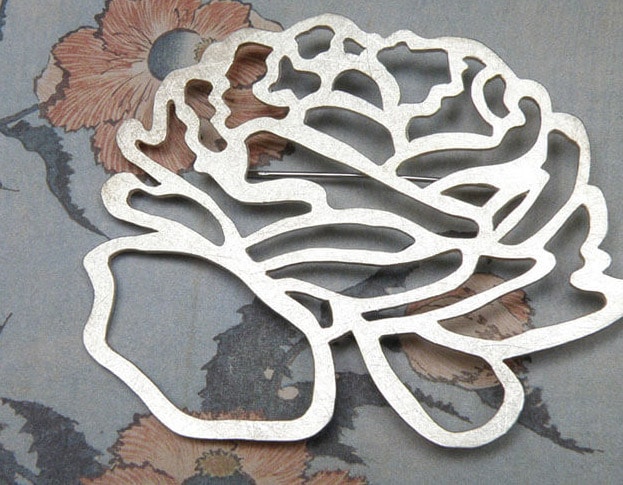 'In bloei' speld met zilveren ranonkel. 'In bloom' pin with silver flower. Uit het Oogst atelier Amsterdam.