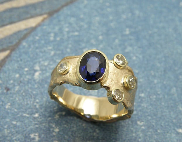 Blog about sapphire. Ring ‘Erosion’ ring with texture made of heirloom yellow gold, diamonds and sapphire from a beloved, but worn out, ring. Oogst studio in Amsterdam.