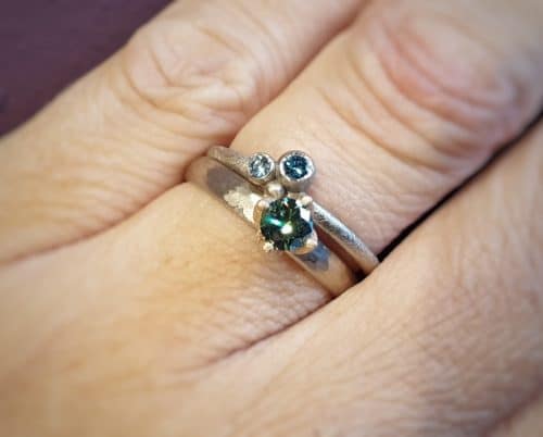 White gold 'Berry' ring with blue diamonds and a white gold ring 'Rhythm' with green diamond. Oogst goldsmith studio Amsterdam