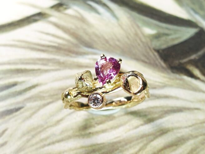 Geelgouden 'Twist' ring met een roségouden perzik, een kristal en 0,65 crt peergeslepen roze korund en 0,11 crt diamant brown . Ontwerp van Oogst goudsmid in Amsterdam voor de Amorf vs Kristallijn collectie.