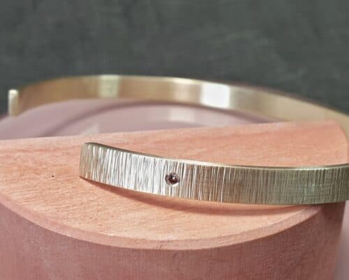 Yellow golden cuff bracelet Rhythm with stripey hammering and a brown diamond. Design by Oogst Jewellery in Amsterdam