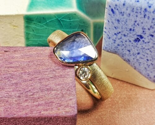Gedenksieraad 'Verzameling'. Ring met blauwe saffier en sprankelende diamant op trouwring verwerkt. Herdenkingssieraad van het Oogst atelier.