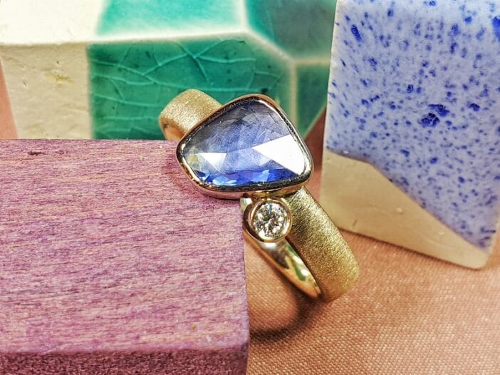 Gedenksieraad 'Verzameling'. Ring met blauwe saffier en sprankelende diamant op trouwring verwerkt. Herdenkingssieraad van het Oogst atelier.