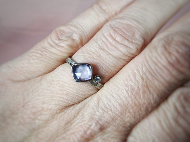 Witgouden 'Deining' ring met violet korund en diamant. Sieraadontwerp van Oogst goudsmeden Amsterdam. Om de vinger