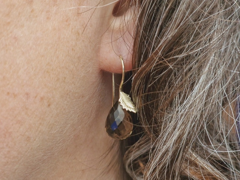 Geelgouden Blaadjes oorbellen met sprankelende rookkwarts druppels. Sieraadontwerp van Oogst Goudsmeden in Amsterdam. In het oor.