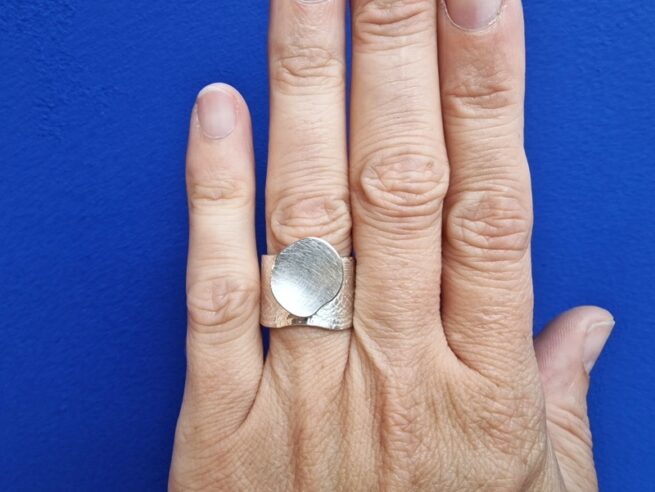 This silver wide ring from the 'Cells' series has a playful mix of patterns and shapes. Oogst Jewellery in Amsterdam. Seen on the finger.