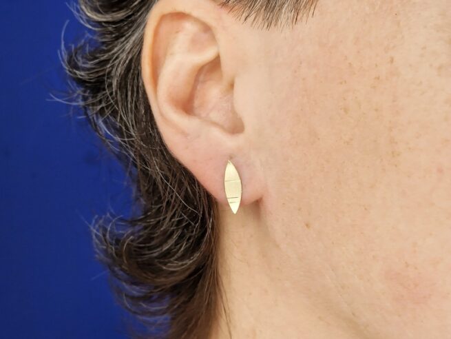 Geelgouden oorstekers, linsvorm met streepjes Mackintosh ornament, in het oor. Oogst Sieraden in Amsterdam.
