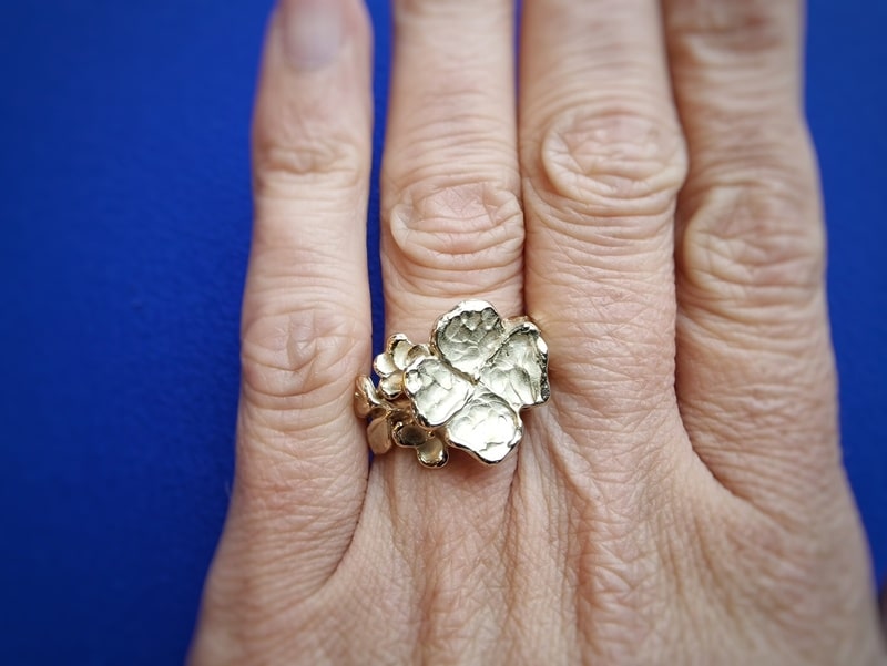 Yellow golden flower ring with playful leaves and a blossom bud. Worn on the finger. Jewellery design by Oogst in Amsterdam