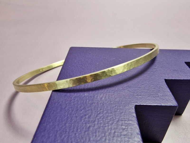 This refined yellow gold bangle 'Rhythm' has an elegant look with it's delicate size and subtile hammering. Designed for someone looking for a timeless and minimal piece. Seen on the side with fine hammering. Oogst Jewellery in Amsterdam.