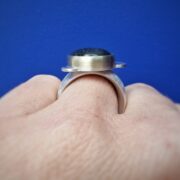 Zilveren edelsteenring met Labradoriet, in geelgoud gezet met wolk motief. Stoere robuuste zilveren ring. Oogst Goudsmeden in Amsterdam. Om de vinger gezien van de zijkant.