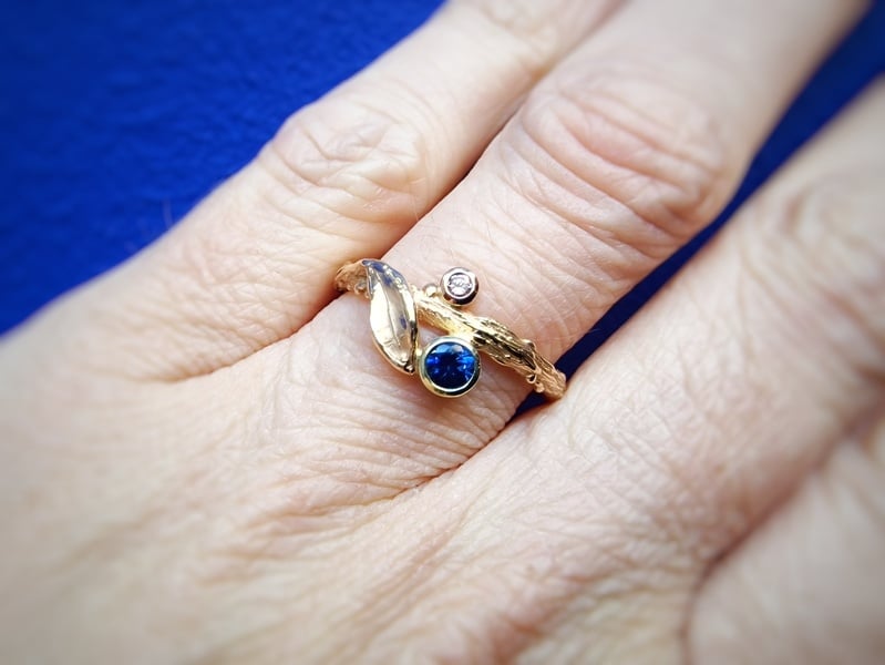 Ring with a sapphire and a diamond. Twig with leaf in rosé gold. One-of-a-kind ring created by Oogst Jewellery. Seen on the finger.
