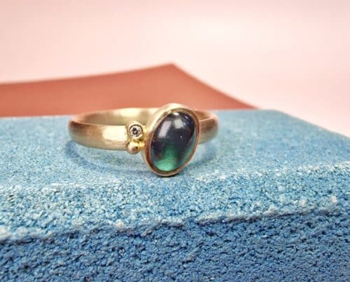 Ring 'Rhythm' with bold hammering, an oval cabochon cut petrol green tourmaline, a 0,02 ct diamond, and a small berry. Created from own rosé gold. Handmade at the Oogst studio