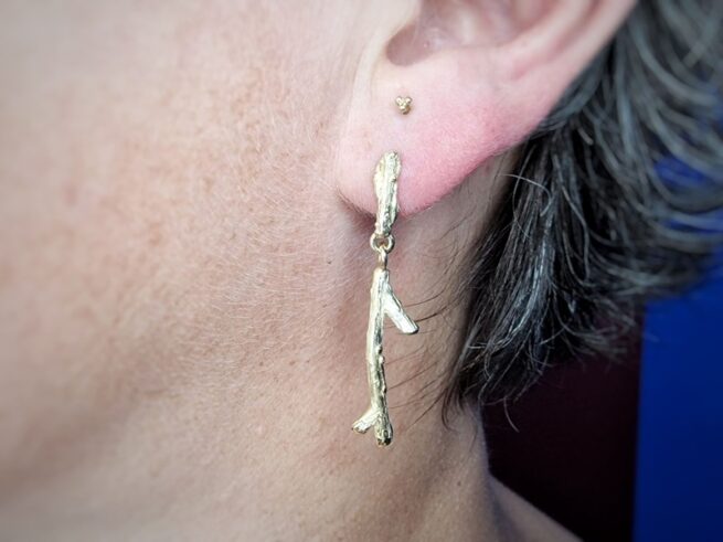 Geelgouden oorsieraden takjes, in het oor. Uit de 'Boomgaard' serie van Oogst Goudsmeden.
