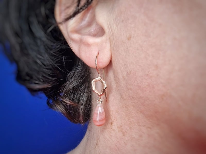 Roodgouden Amorf oorsieraden met oranje agaat met krul, in het oor. Uit het Oogst atelier.