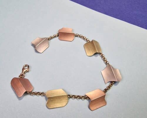 Roodgouden armband 'Vouwen' met witgouden, roségouden en geelgouden bedels. Gevouwen vormen en speelse mix van kleuren. Ontwerp van Oogst goudsmid in Amsterdam.
